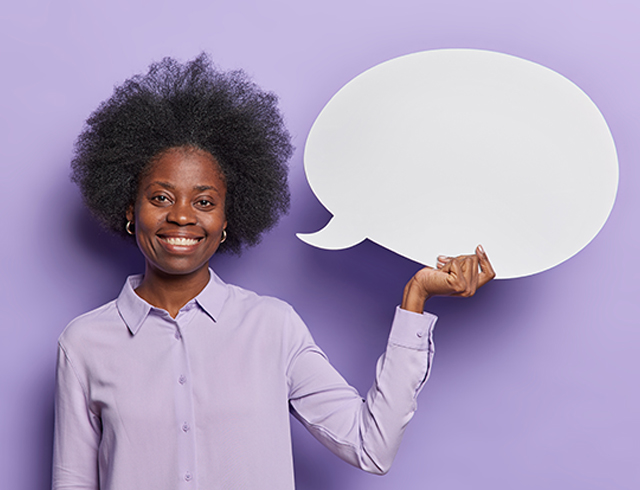 Horizontal shot of cheerful African American businesswoman smiles toothily wears formal shirt holds blank white speech bubble suggests to write your text here isolated over purple background